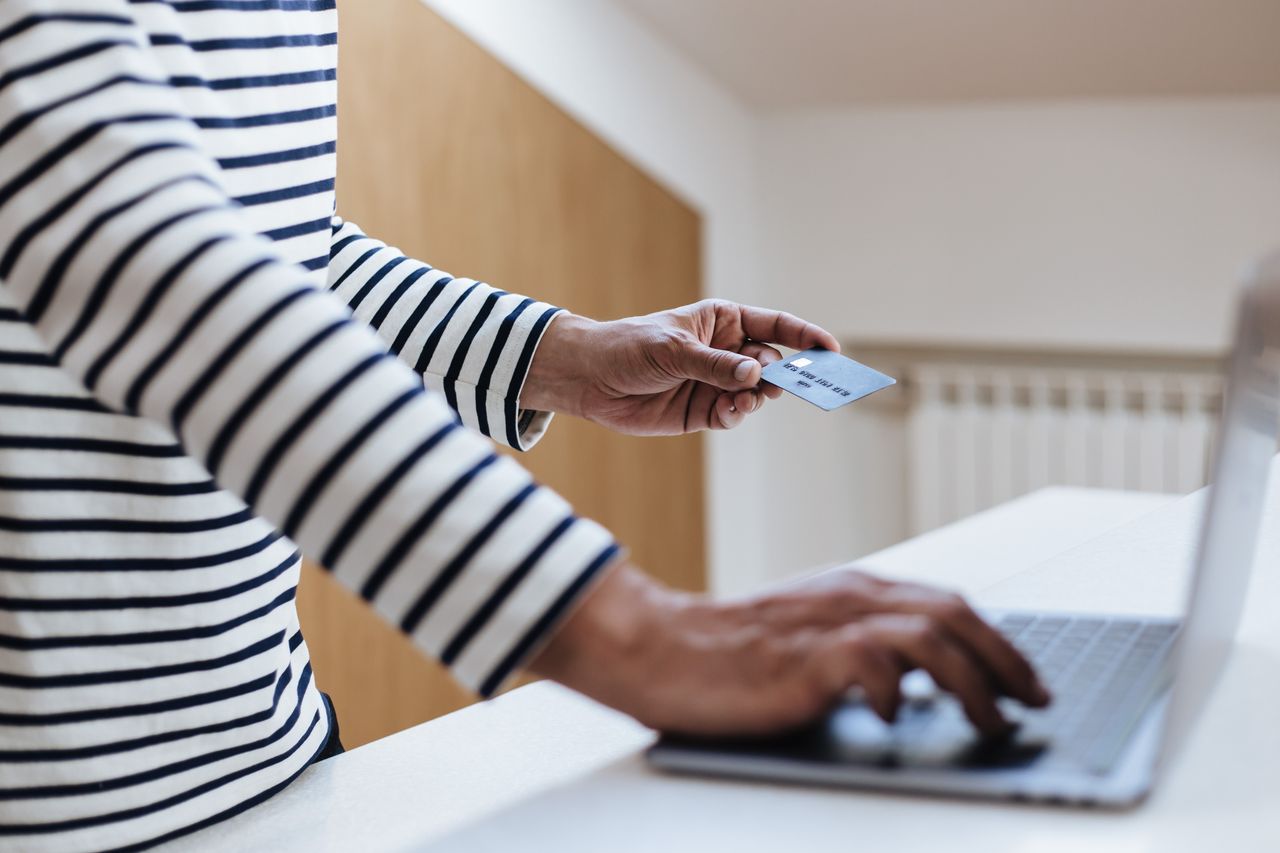Person using a credit card for online shopping on a laptop indoors.