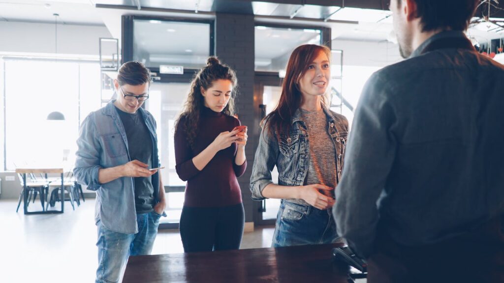 Three young adults in line at a café, interacting with the barista.