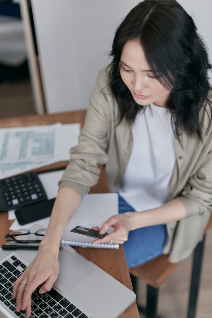 A woman making an online payment using a laptop, credit card, and documents.